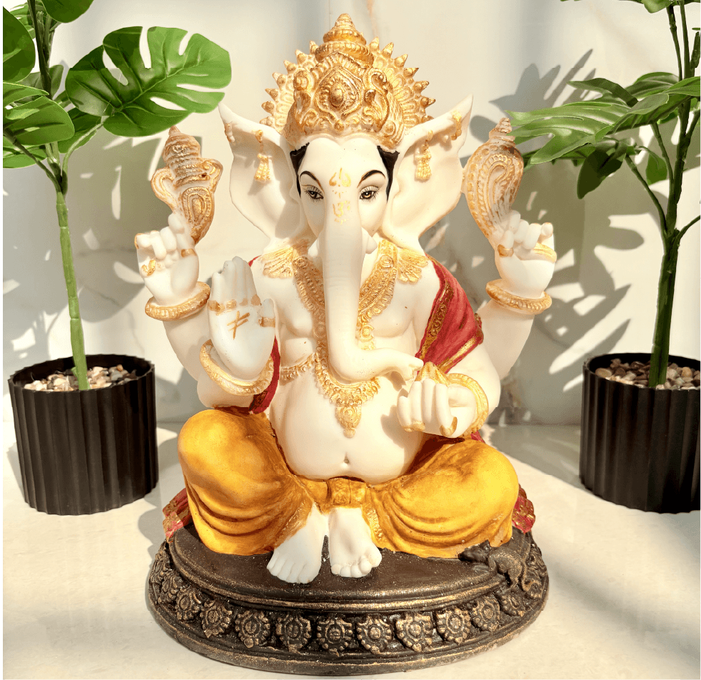 Decorative statue of a seated figure with gold and white details, surrounded by plants.