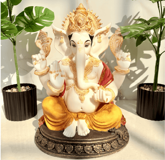 Decorative statue of a seated figure with gold and white details, surrounded by plants.