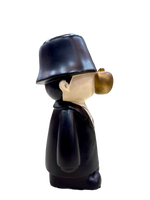 Left side view of 9.5 inch resin figurine with black coat, bucket hat, golden apple face and gold dollar chain, quirky home décor collectible
