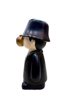 side view of 9.5 inch resin figurine with black coat, bucket hat, golden apple face and gold dollar chain, quirky home décor collectible