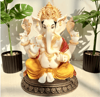 Decorative statue of a seated figure with gold and white details, surrounded by plants.